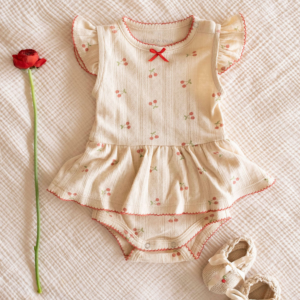 Baby cherry romper and booties on a muslin cloth crib sheet that makes for a unique baby gift