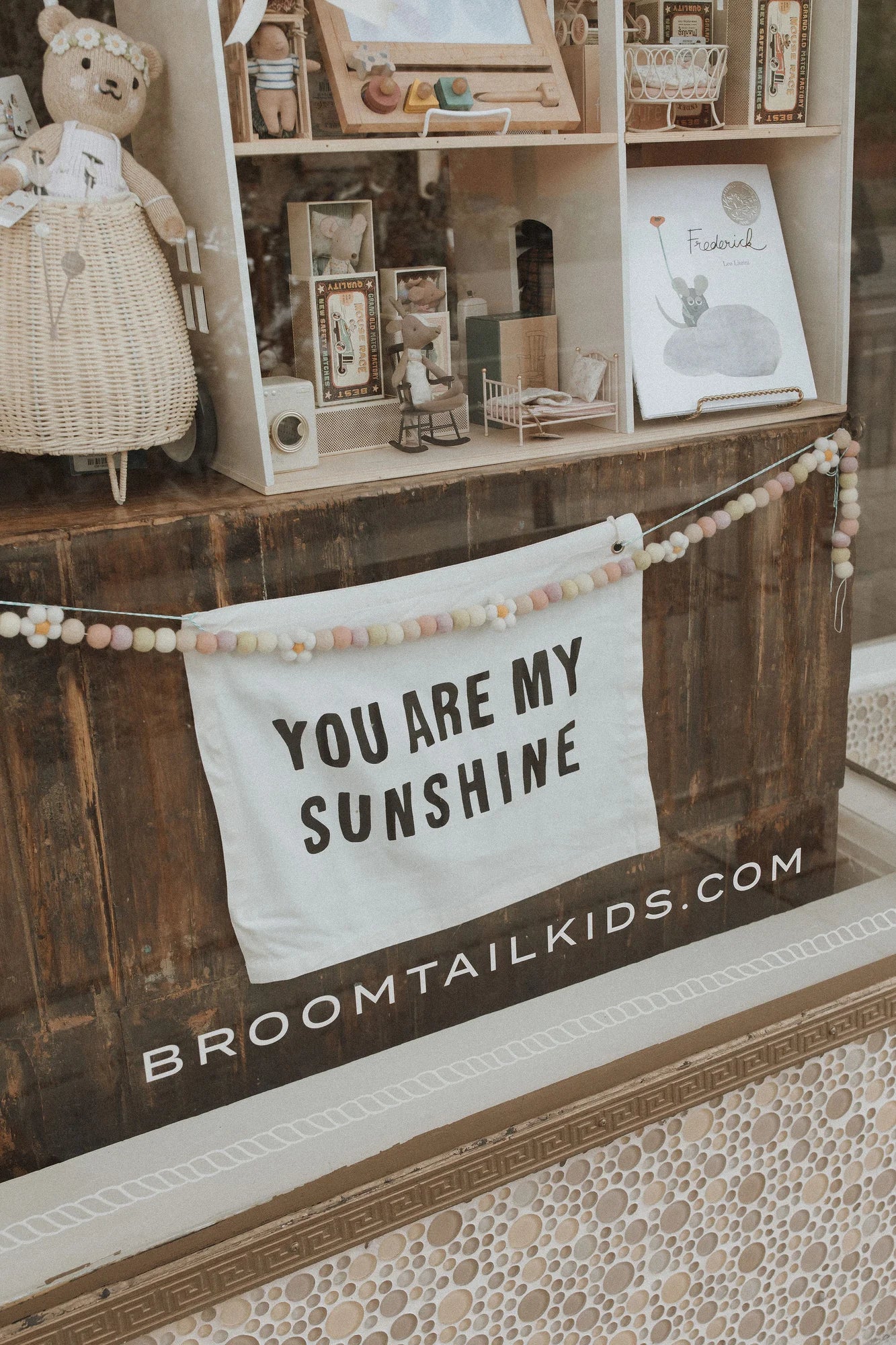 Broomtail kids window display with a sign that says "you ar my sunshine" hanging in front of a Broomtail's collection of unique baby and kids gifts.