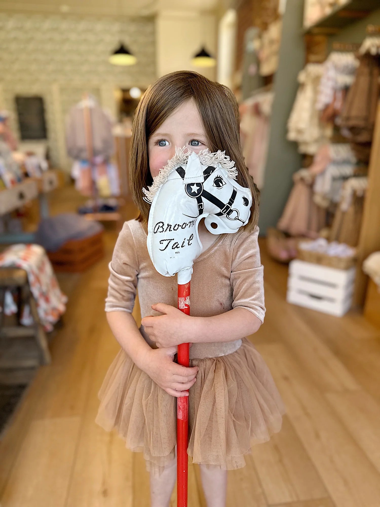 Young girl holding a broom with a horse head and harness design inside Broomtail in Denver Colorado