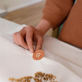 Hand holding a round orange sticker with a letter 'B' for "Broomtail" as part of the signature gift wrapping service offered in-store and online