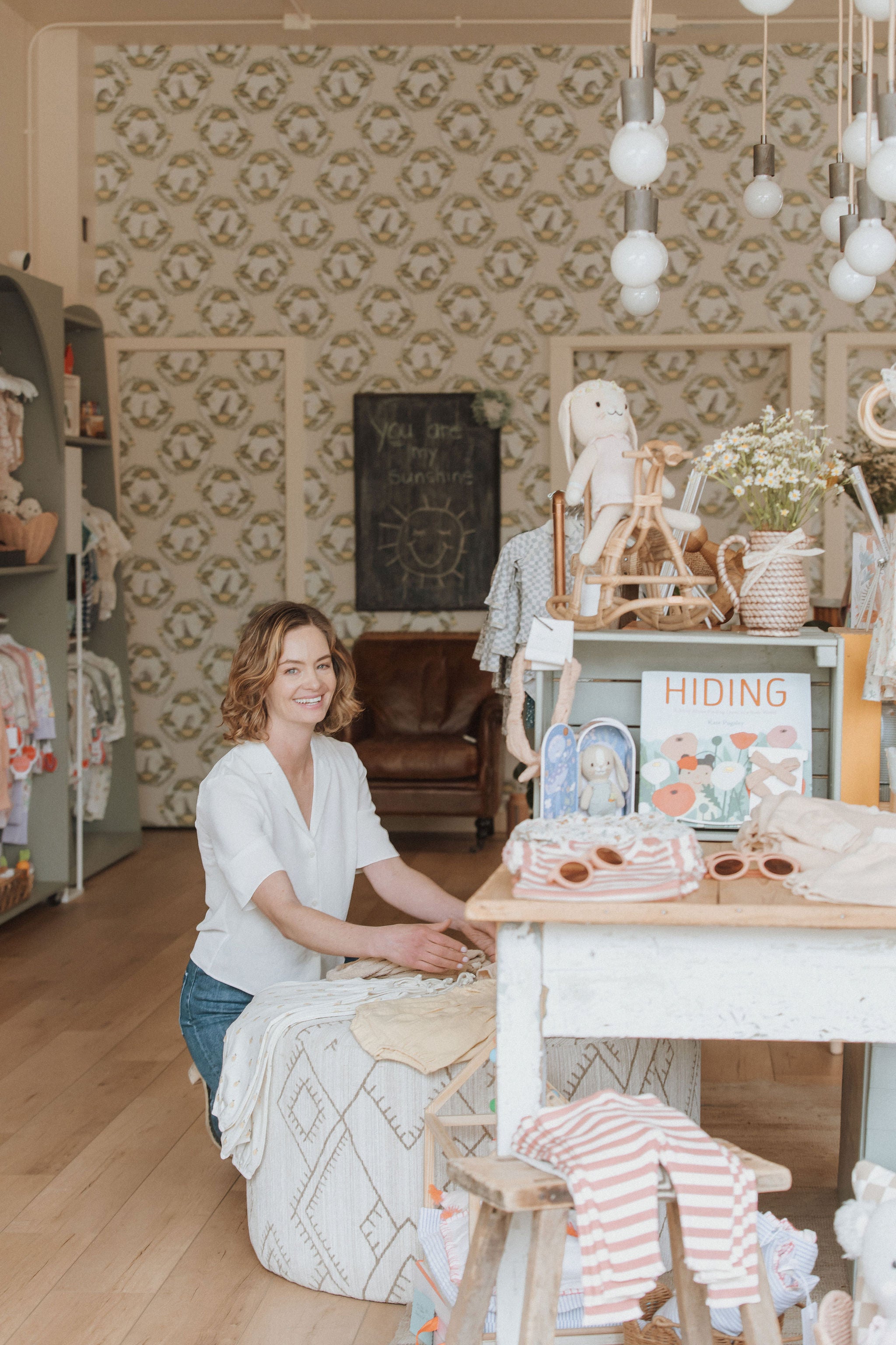 Kids boutique founder, Maris, next to a table of BPA-free baby toys and accessories at Broomtail.