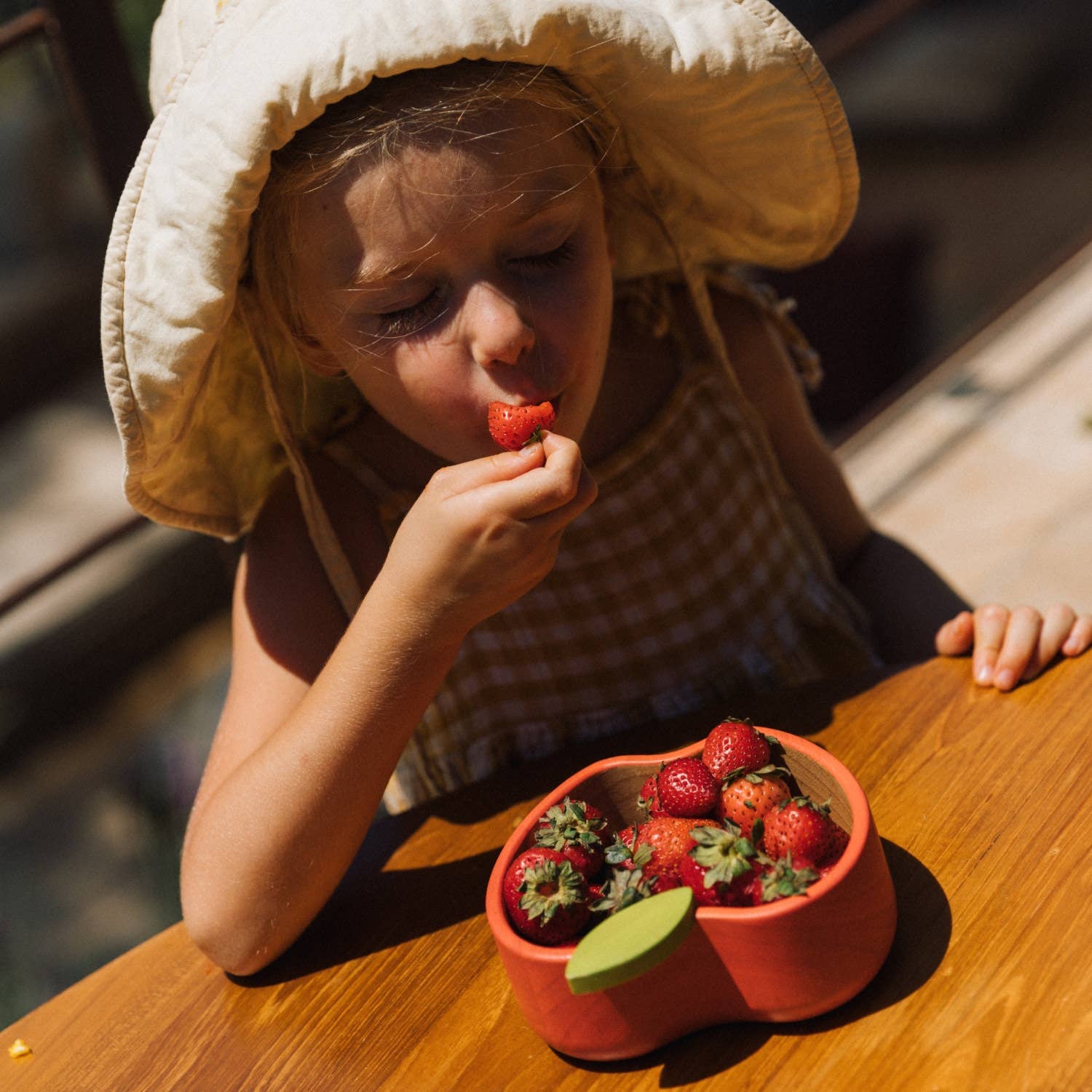 Girl eaying strawberries out of a strawberry shaped bowl while wearing ethically sourced children's clothing and accessories.